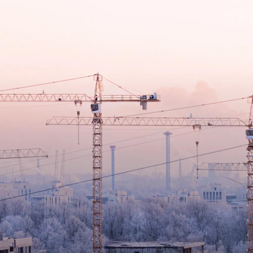 Aerial view of multiple cranes working on half-built buildings in a snowy city.