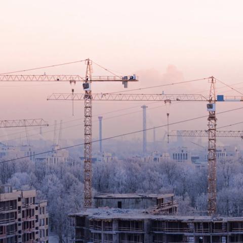 Aerial view of multiple cranes working on half-built buildings in a snowy city.