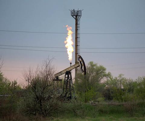 An oil pumping jack, also known as a 'nodding donkey' and flare stack in an oil field in Russia. Photographer: Andrey Rudakov/Bloomberg