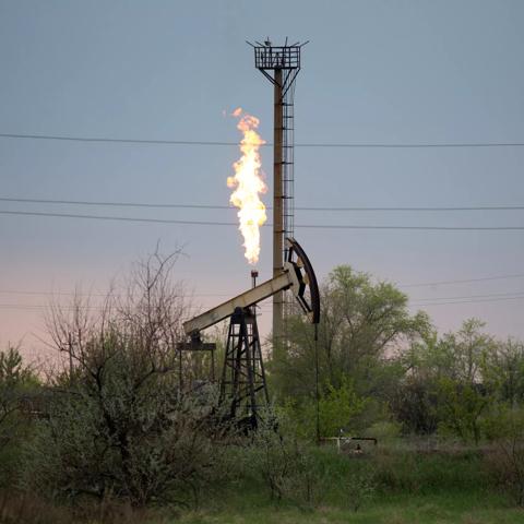 An oil pumping jack, also known as a 'nodding donkey' and flare stack in an oil field in Russia. Photographer: Andrey Rudakov/Bloomberg