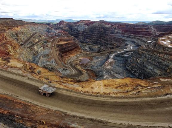 Open pit copper mine in Riotinto, (Huelva, SW Spain) as seen from the viewpoint outside. One loaded dumptruck climbs the hauling road while the pit behind it shows all the red colours from different minerals. Image taken around noon in  a cloudy winter morning