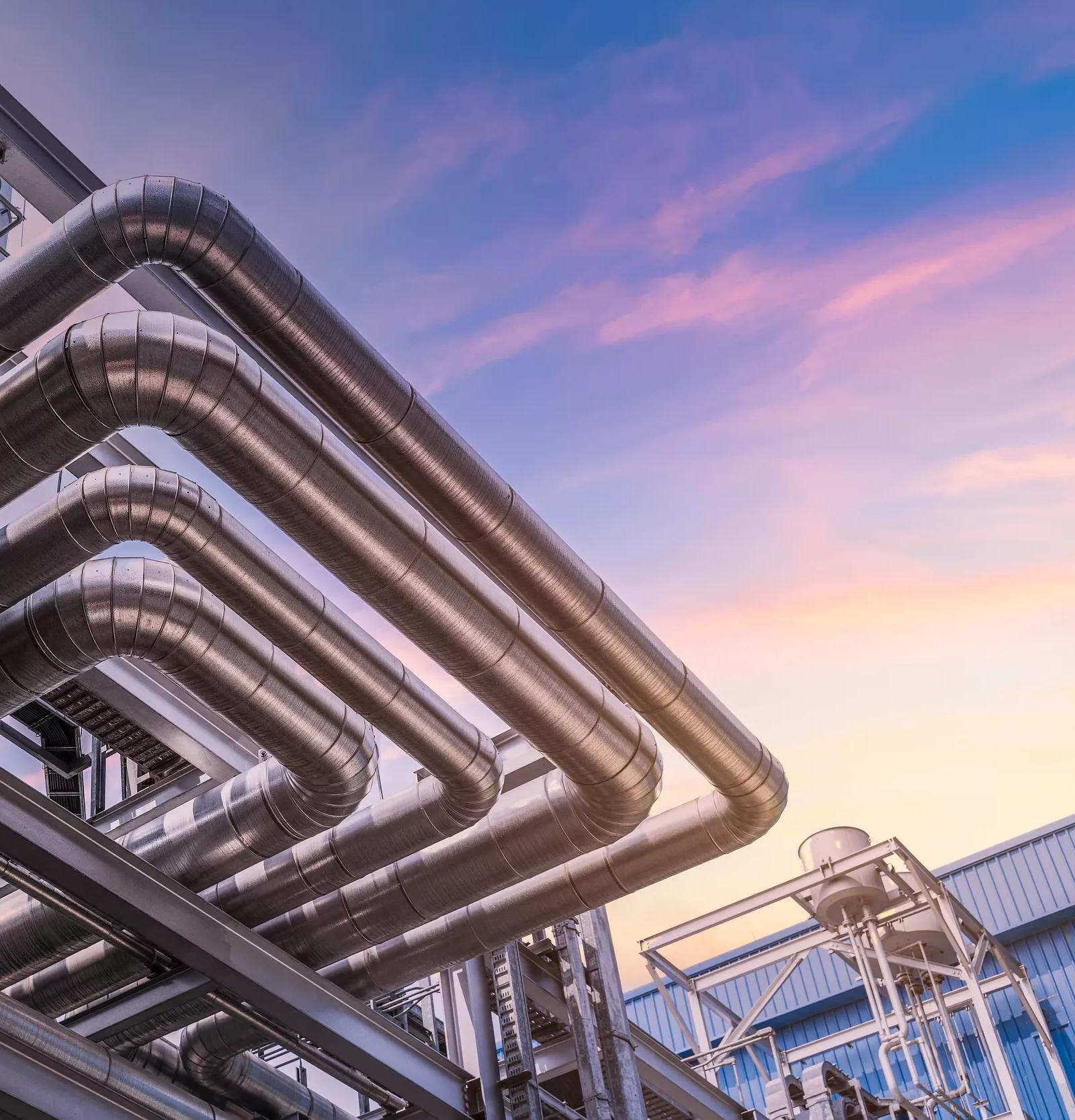 Ground-view of industrial metal pipes running horizontally and vertically along a steel structure.