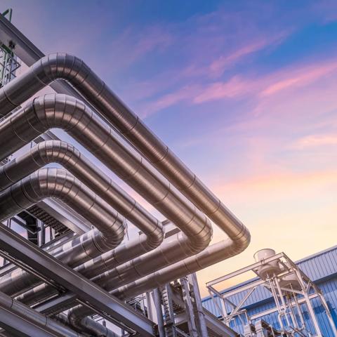 Ground-view of industrial metal pipes running horizontally and vertically along a steel structure.