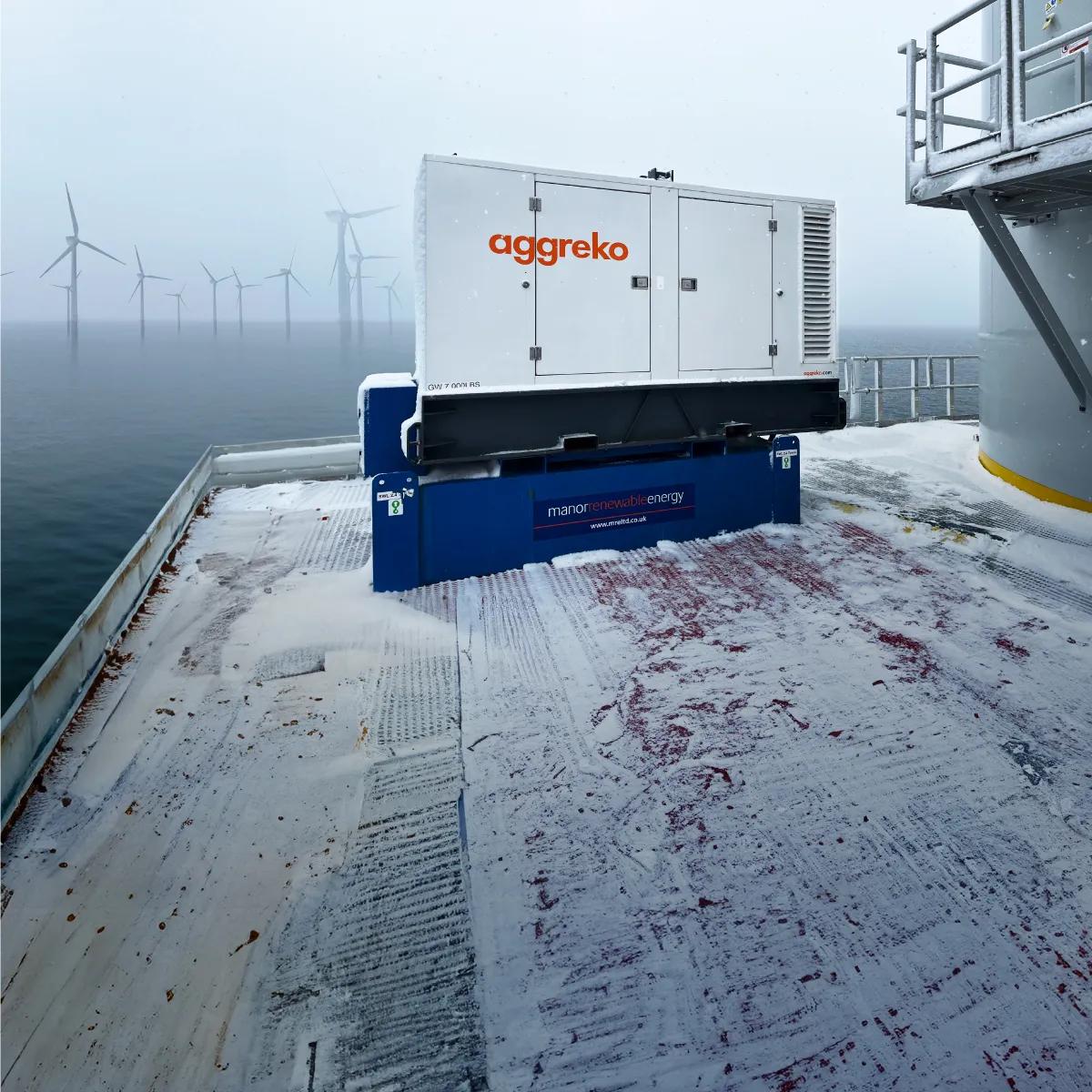 A foggy seascape with wind turbines in the distance, featuring an Aggreko industrial generator in the foreground on a platform.