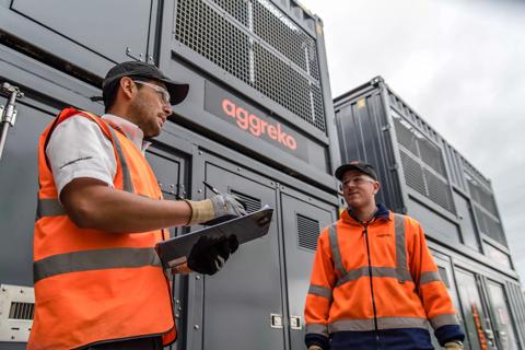 2 workers in uniform stand in front of multiple stacked industrial units.