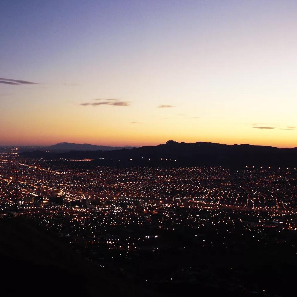 A panoramic, high-angle view of a vast city at dusk, with thousands of lights illuminating the urban landscape.