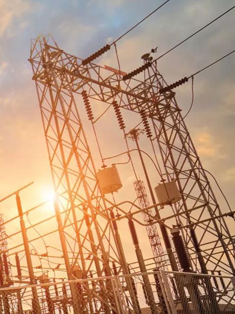 A complex electrical substation with transmission lines and equipment silhouetted against a bright sunset.