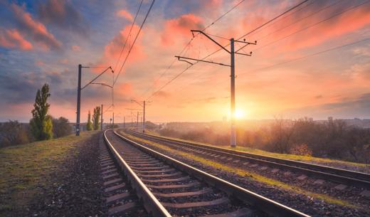 Railroad and beautiful sky at sunset. Industrial landscape with railway station, colorful blue sky with red clouds, trees and green grass, yellow sunlight in summer. Railway junction. Heavy industry