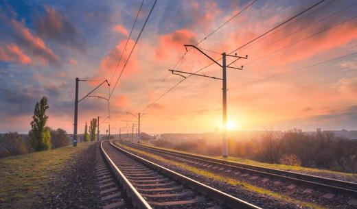 Railroad and beautiful sky at sunset. Industrial landscape with railway station, colorful blue sky with red clouds, trees and green grass, yellow sunlight in summer. Railway junction. Heavy industry