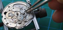 watchmaker reparing vintage watch mechanism taking small gear with tweezers