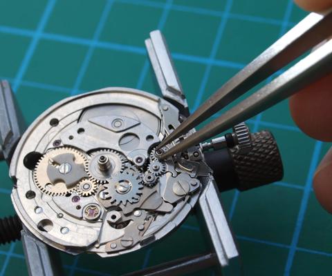 watchmaker reparing vintage watch mechanism taking small gear with tweezers