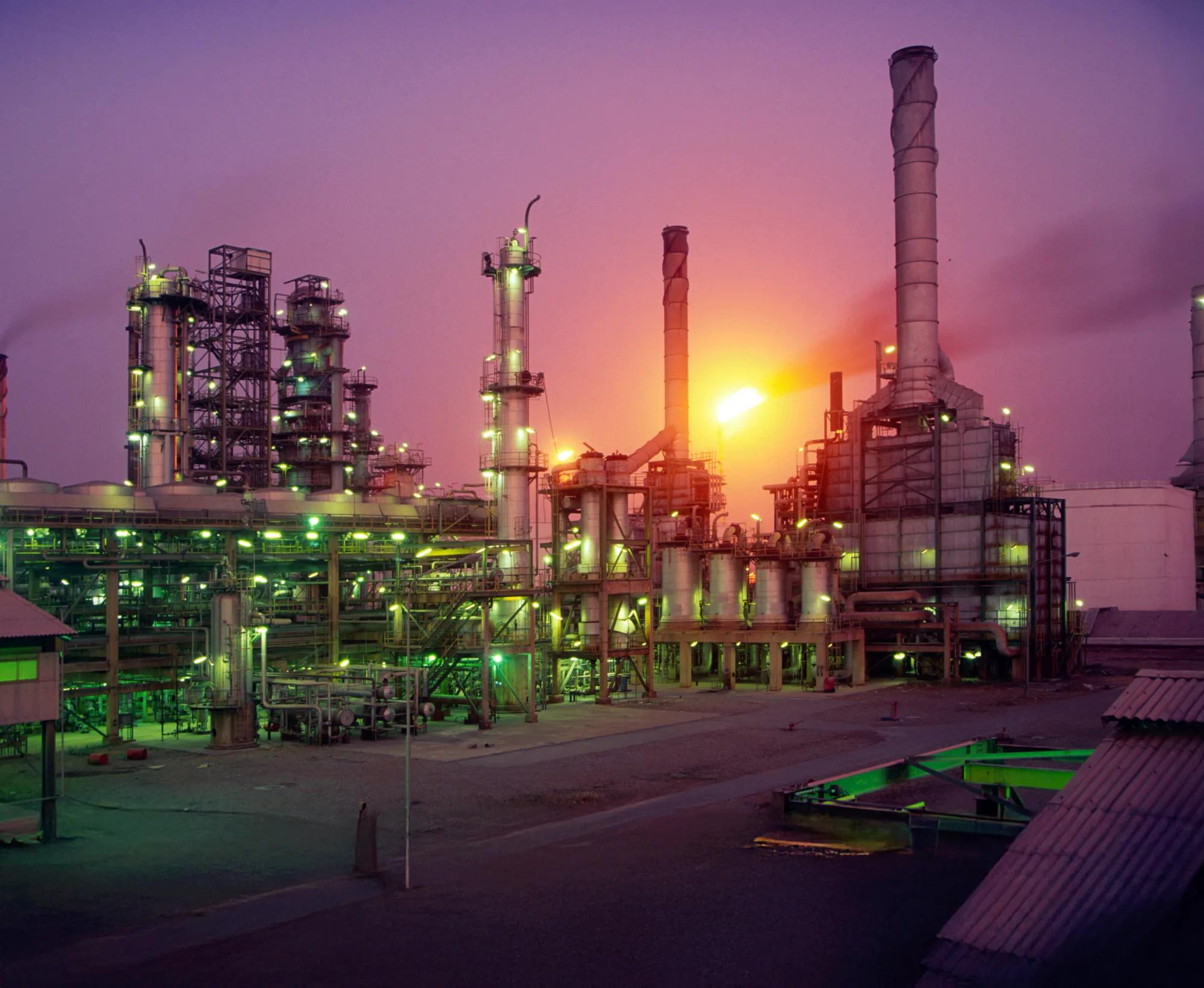 A wide shot of a large industrial complex or refinery at dusk or night.