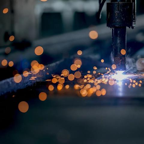 A close-up, dark image of a welding operation, showing a shower of bright orange sparks against a blurry industrial background.