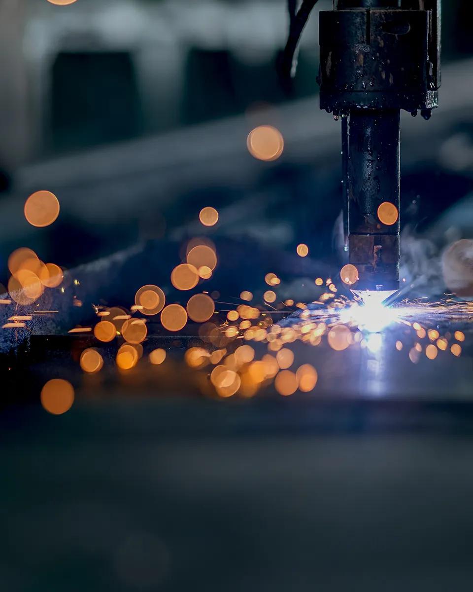 Gros plan sur une image sombre d’une opération de soudage, montrant une douche d’étincelles orange vif sur un fond industriel flou.