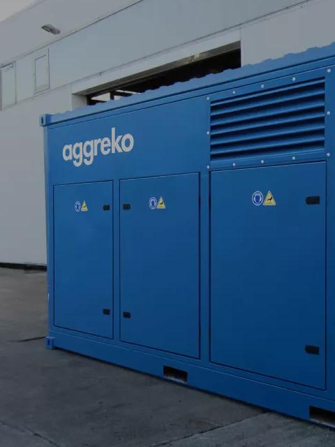 A blue Aggreko electric OFA compressor on the patio between industrial buildings