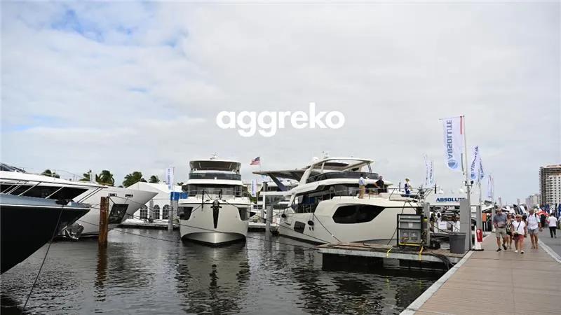 Several civilians are walking down a pier with several yachts docked on the side.
