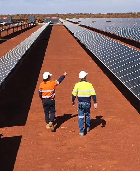 Aerial view of 2 workers in uniform walking by multiple rows of solar panels. 