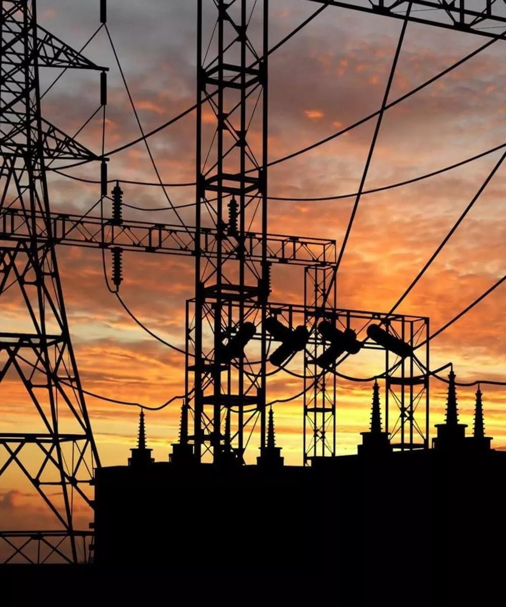 The complex latticework of high-voltage transmission towers, silhouetted against a vibrant orange sunset sky.