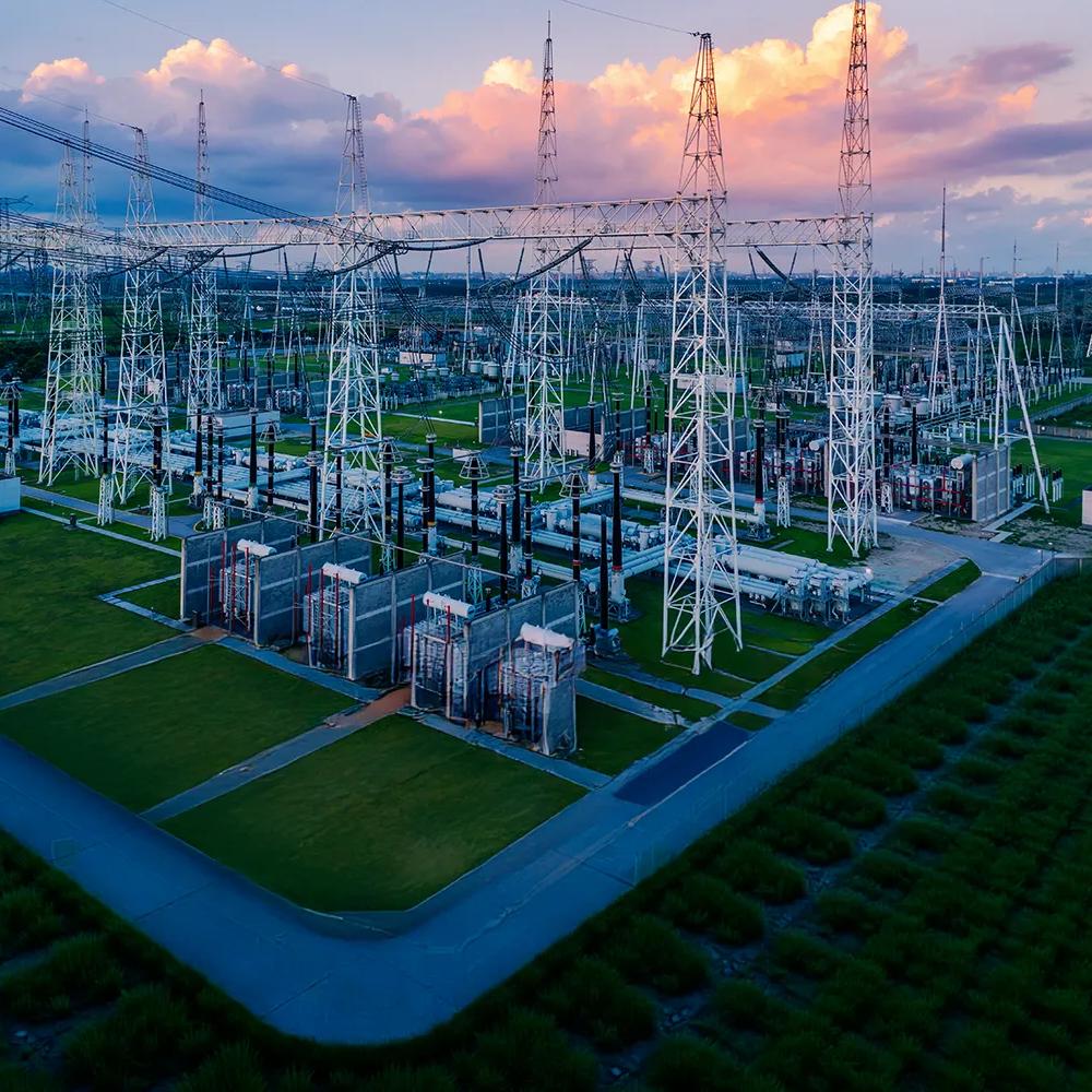 View of an electrical plant in a green field against a cloudy sky with pink tones.