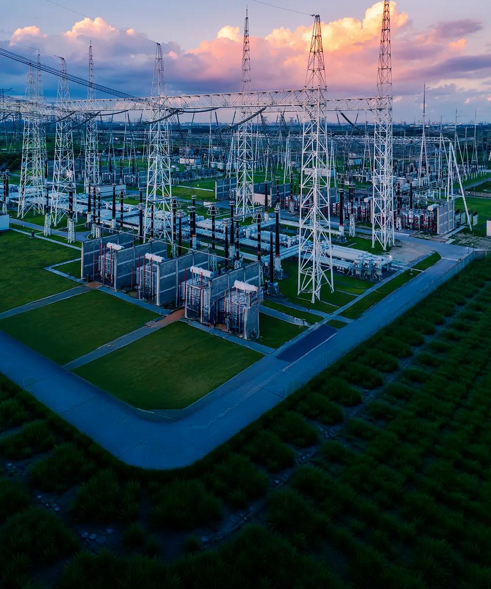 Vue d’une centrale électrique dans un champ vert sous un ciel nuageux avec des tons roses.