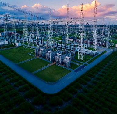 View of an electrical plant in a green field against a cloudy sky with pink tones.