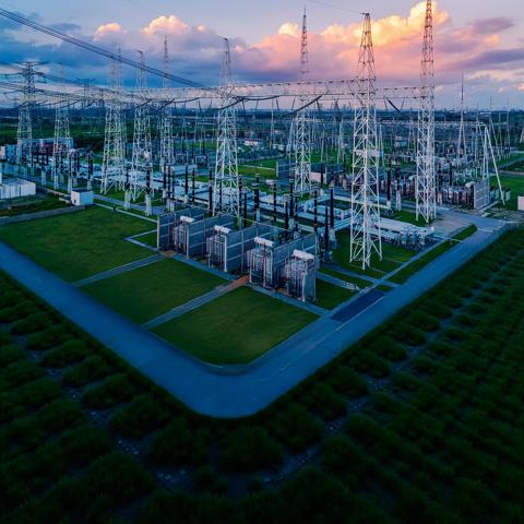 View of an electrical plant in a green field against a cloudy sky with pink tones.