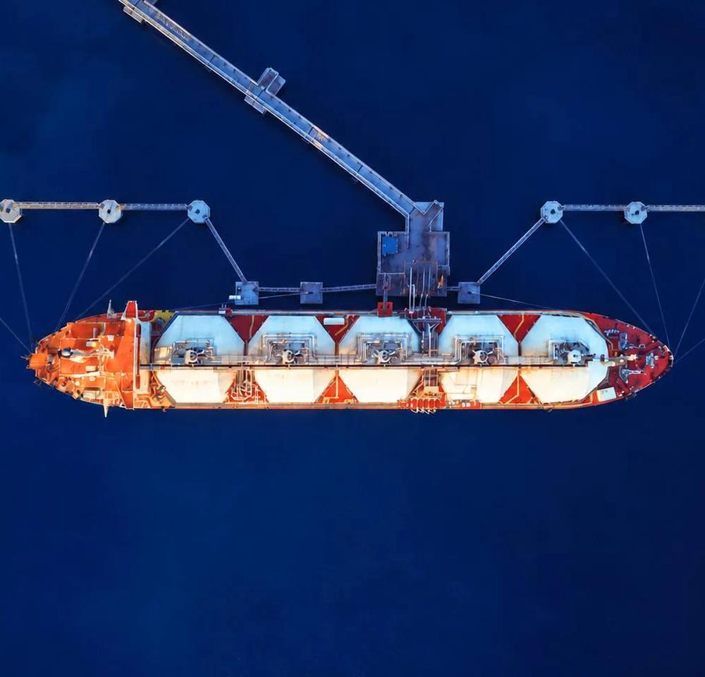 A large orange and white cargo ship with tanks, suspended above deep blue water, showcasing shipping and marine technology.