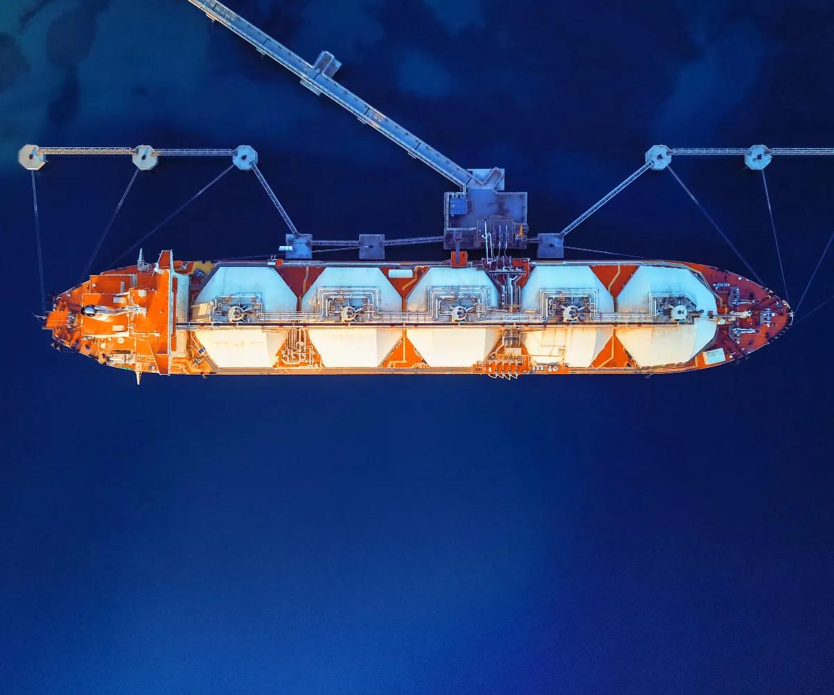 A large orange and white cargo ship with tanks, suspended above deep blue water, showcasing shipping and marine technology.