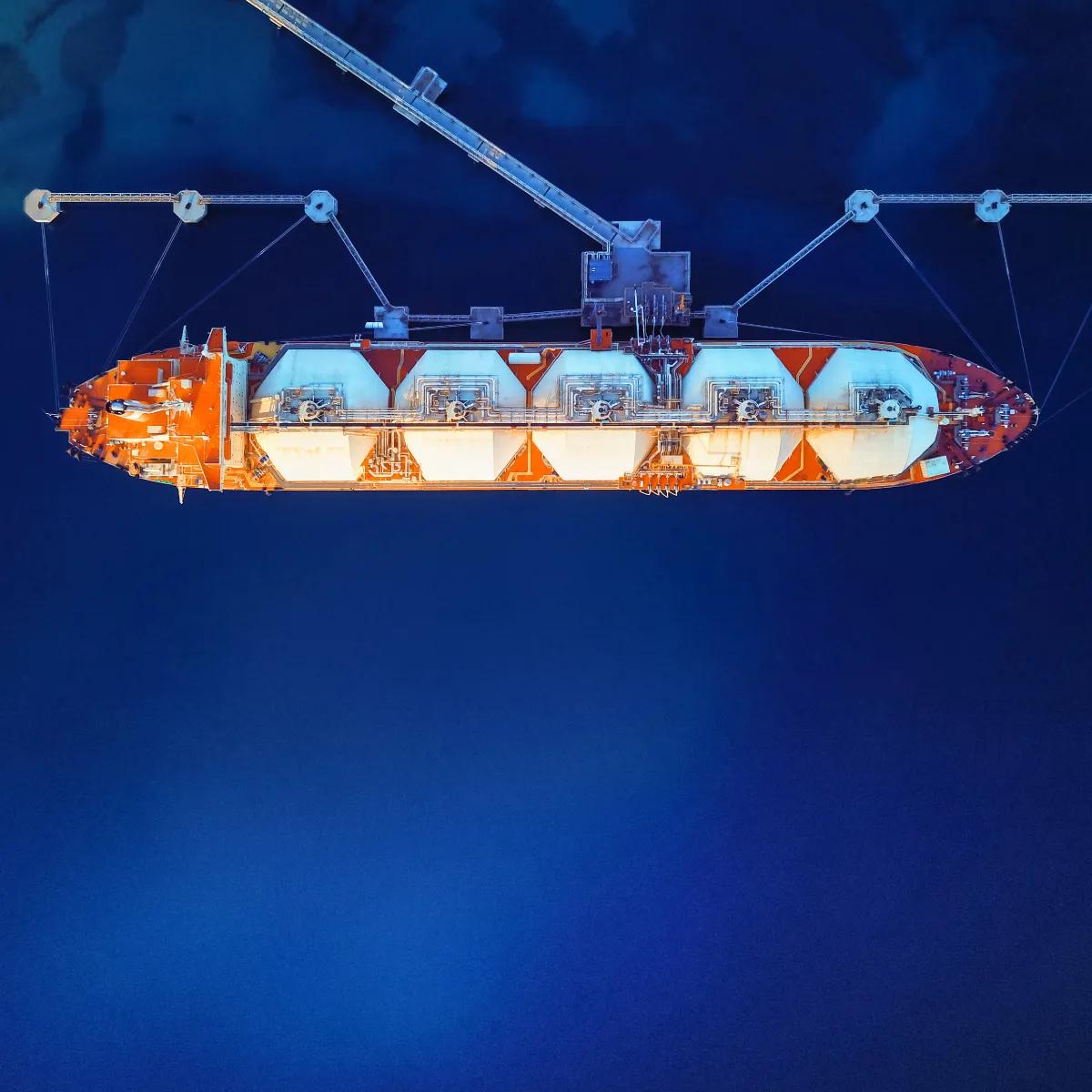 A large orange and white cargo ship with tanks, suspended above deep blue water, showcasing shipping and marine technology.