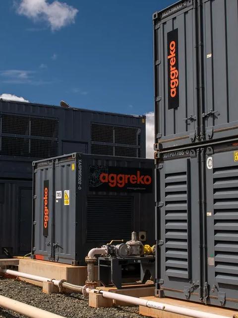 View of a worker in uniform walking by multiple rows of double-stacked industrial units with the Sun setting in the background.