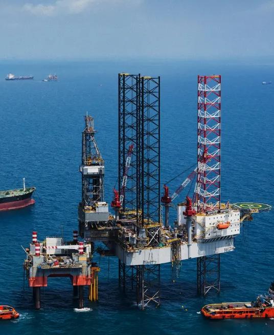 Offshore oil drilling platform with cranes, equipment, and support vessels in blue water.
