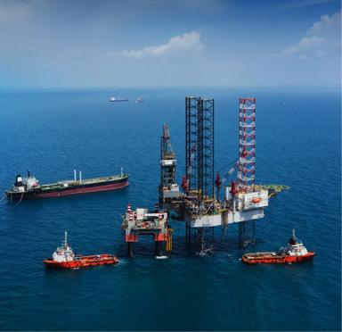Offshore oil drilling platform with cranes, equipment, and support vessels in blue water.