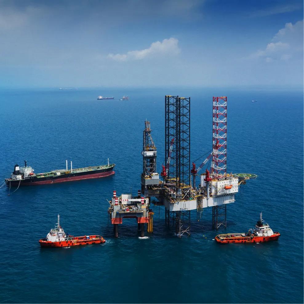 Offshore oil drilling platform with cranes, equipment, and support vessels in blue water.