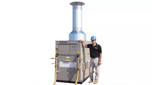 A person stands next to a hydronic heating unit with a tall metal exhaust. The person is wearing a blue hard hat and black shirt.
