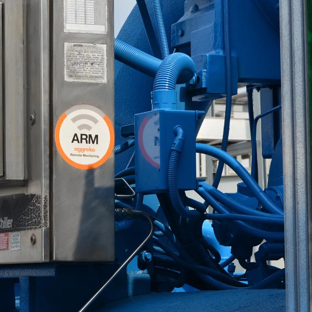 A gray industrial tank with the logo "Aggreko" on it, part of a larger machinery setup, featuring pipes and control panels.