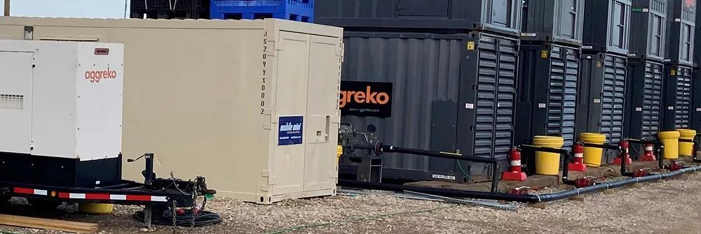 An Aggreko black generator on gravel yard next to another piece of equipment