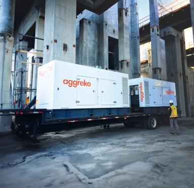 A large trailer-mounted power generator in an industrial setting, with a worker wearing a safety vest nearby.