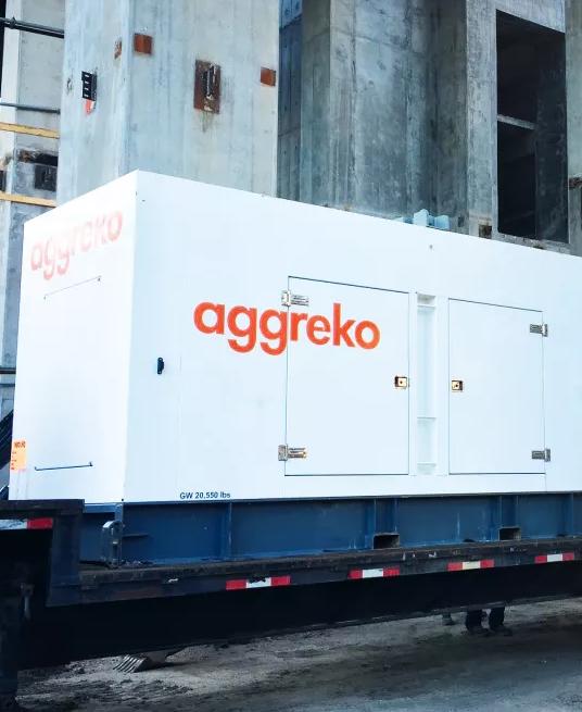 Two trailer-mounted white Aggreko generators at a worksite and a worker next to the equipment