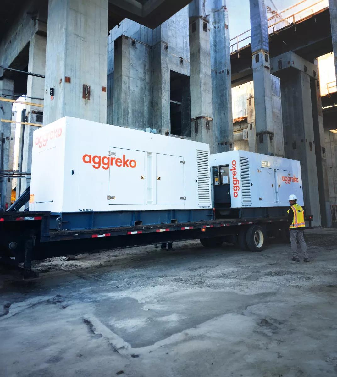 Deux générateurs Aggreko blancs montés sur remorque sur un chantier et un ouvrier à côté de l’équipement