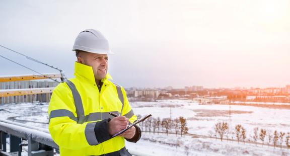 Worker in uniform writing on a clipboard with a snowy background.