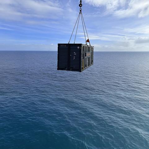 A black Aggreko generator held over the sea