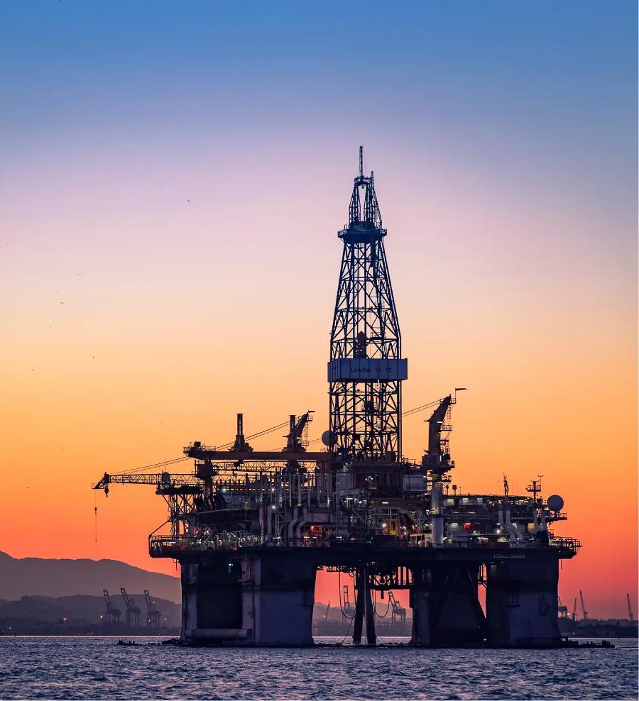 An offshore oil rig silhouetted against a vibrant orange sunset.