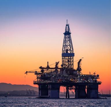 An offshore oil rig silhouetted against a vibrant orange sunset.