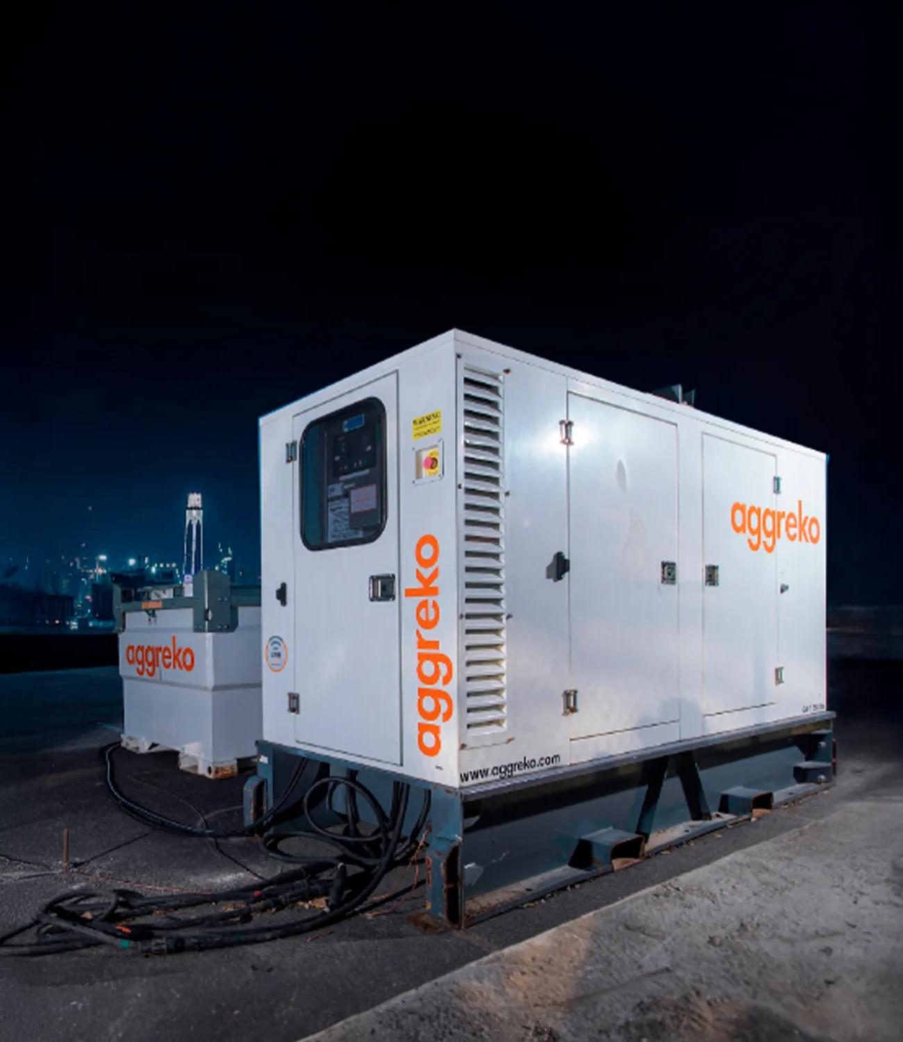 A white Aggreko generator, mounted on a flatbed trailer with cables connected at the base. There's another white, smaller sitting behind.
