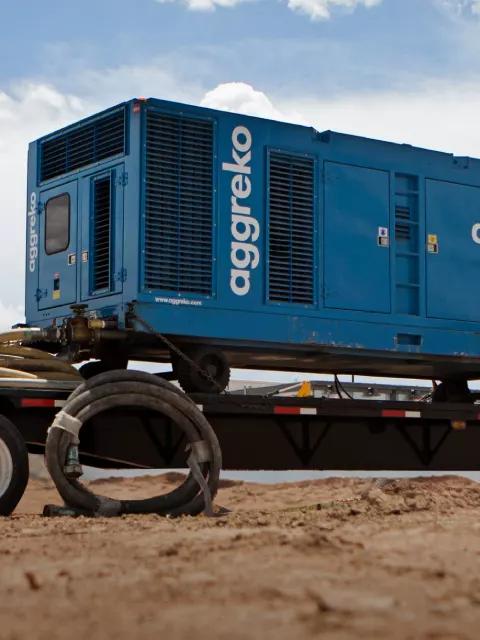 Aggreko industrial equipment transported on a flatbed trailer at a desert site.