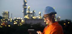 Asian man engineer using digital tablet working late night shift at petroleum oil refinery in industrial estate. Chemical engineering, fuel and power generation, petrochemical factory industry concept