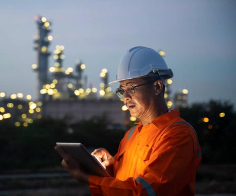 Asian man engineer using digital tablet working late night shift at petroleum oil refinery in industrial estate. Chemical engineering, fuel and power generation, petrochemical factory industry concept