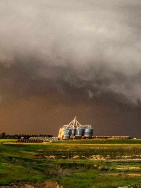 Un ciel dramatique avec des nuages d'orage sombres planant au-dessus d'un paysage herbeux, contrastant avec les zones claires à l'horizon.