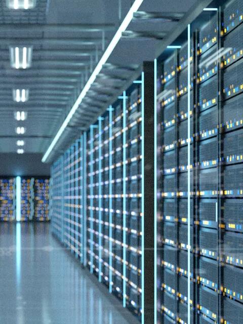 A long, symmetrical perspective view down an aisle in a massive data center server room. The walls are lined with tall, dark server racks, illuminated by vertical strips of cool blue light.