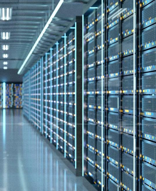 A long, symmetrical perspective view down an aisle in a massive data center server room. The walls are lined with tall, dark server racks, illuminated by vertical strips of cool blue light.
